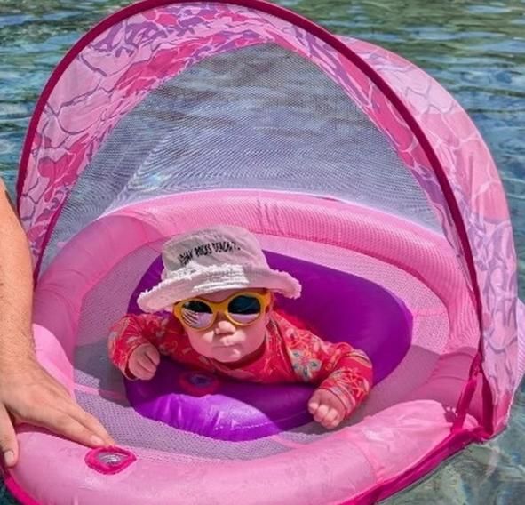 Baby in a pink inflatable pool with canopy surrounded by water and Mokki Click & Change sunglasses