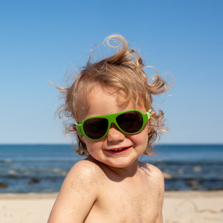 Boy on the beach wearing green Click & Change sunglasses for kids 2-5 years