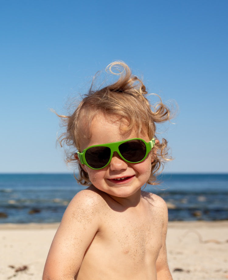 Gutt på stranda med grønne Click & Change-solbriller for barn