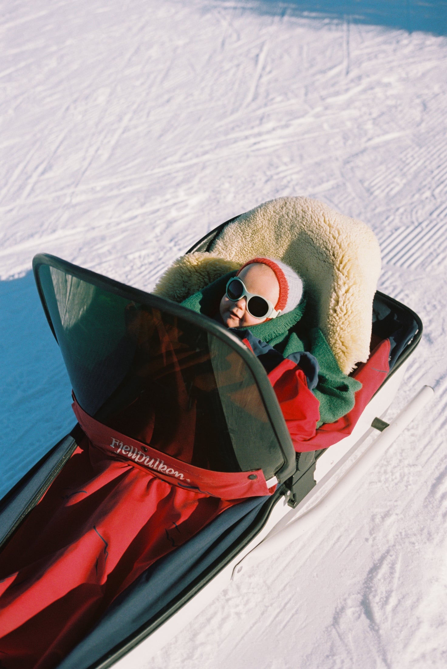 Baby sitting in a pulk with Mokki Click & Change sunglasses on a snowy landscape