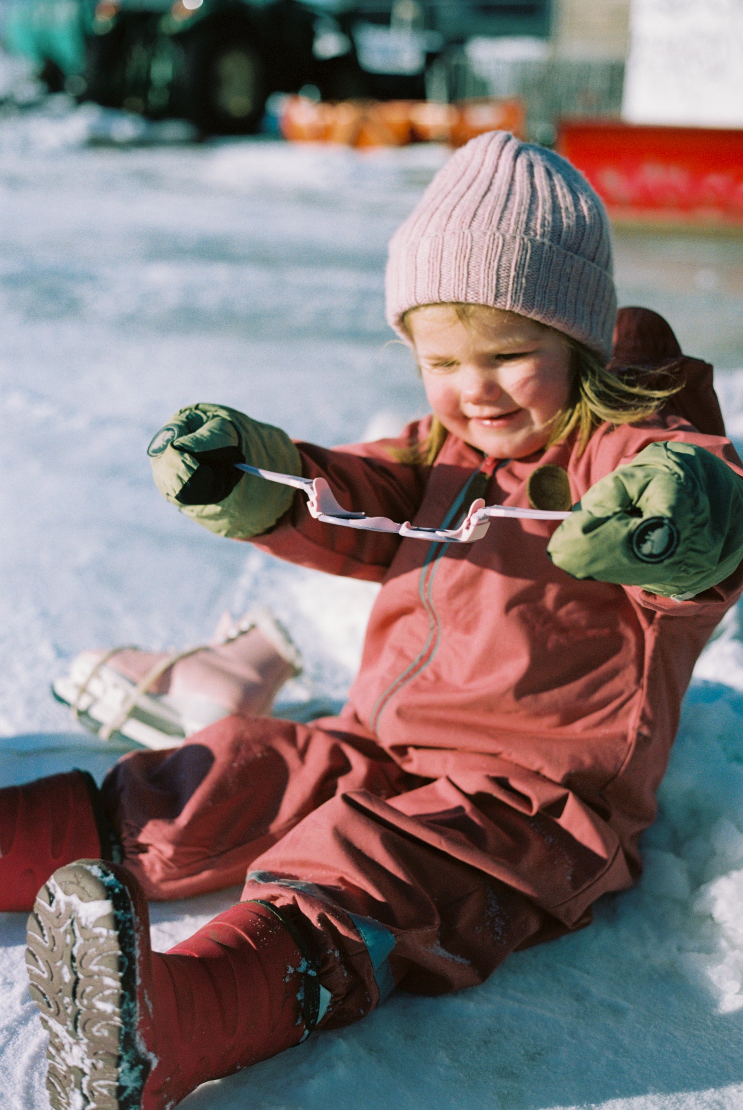 Child in winter clothing sitting on ice, showing how ultra-flexible the Mokki Click & Change sunglasses are