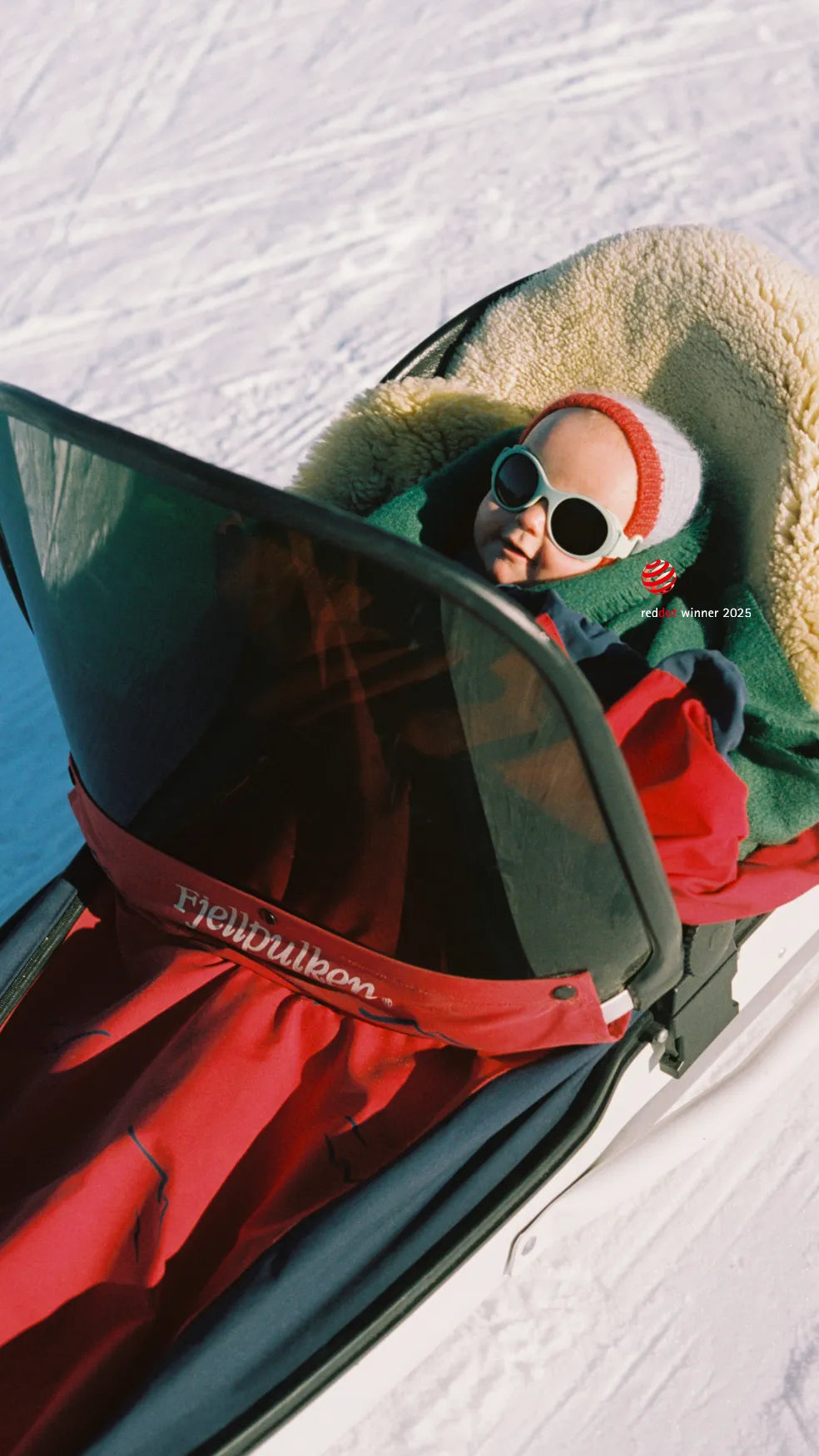 Baby wearing Mokki Click & Change sunglasses laying in a pulk surrounded by snow.