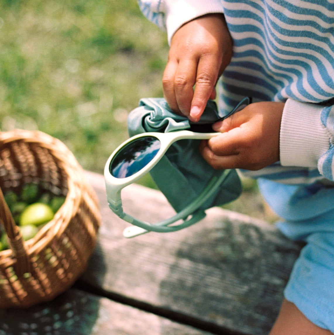 Child in striped shirt and shorts holding  green Click & Change sunglasses.