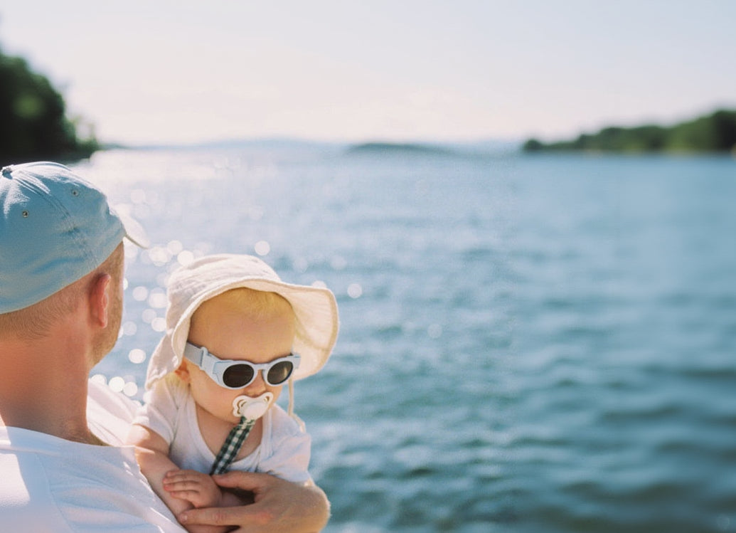 Father holding his baby that is wearing Mokki Click & Change sunglasses.