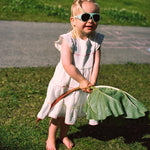 Child in a white dress holding a large leafy vegetable outdoors on grass wearing Click & Change sunglasses