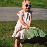 Child in a white dress holding a large leafy vegetable outdoors on grass wearing Click & Change sunglasses