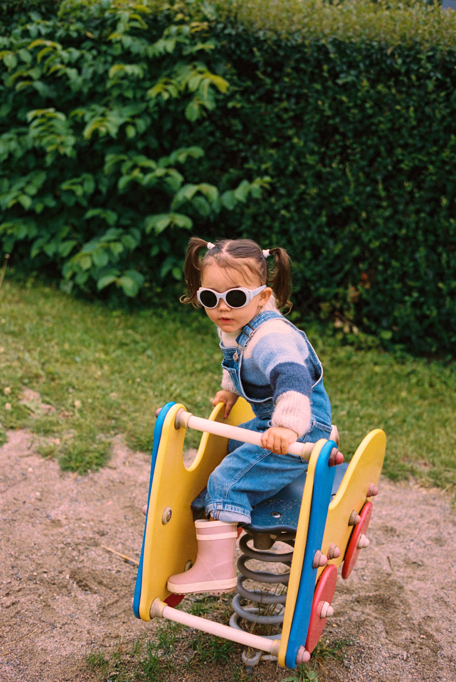 Child on a spring toy in a park setting wearing Mokki sunglasses