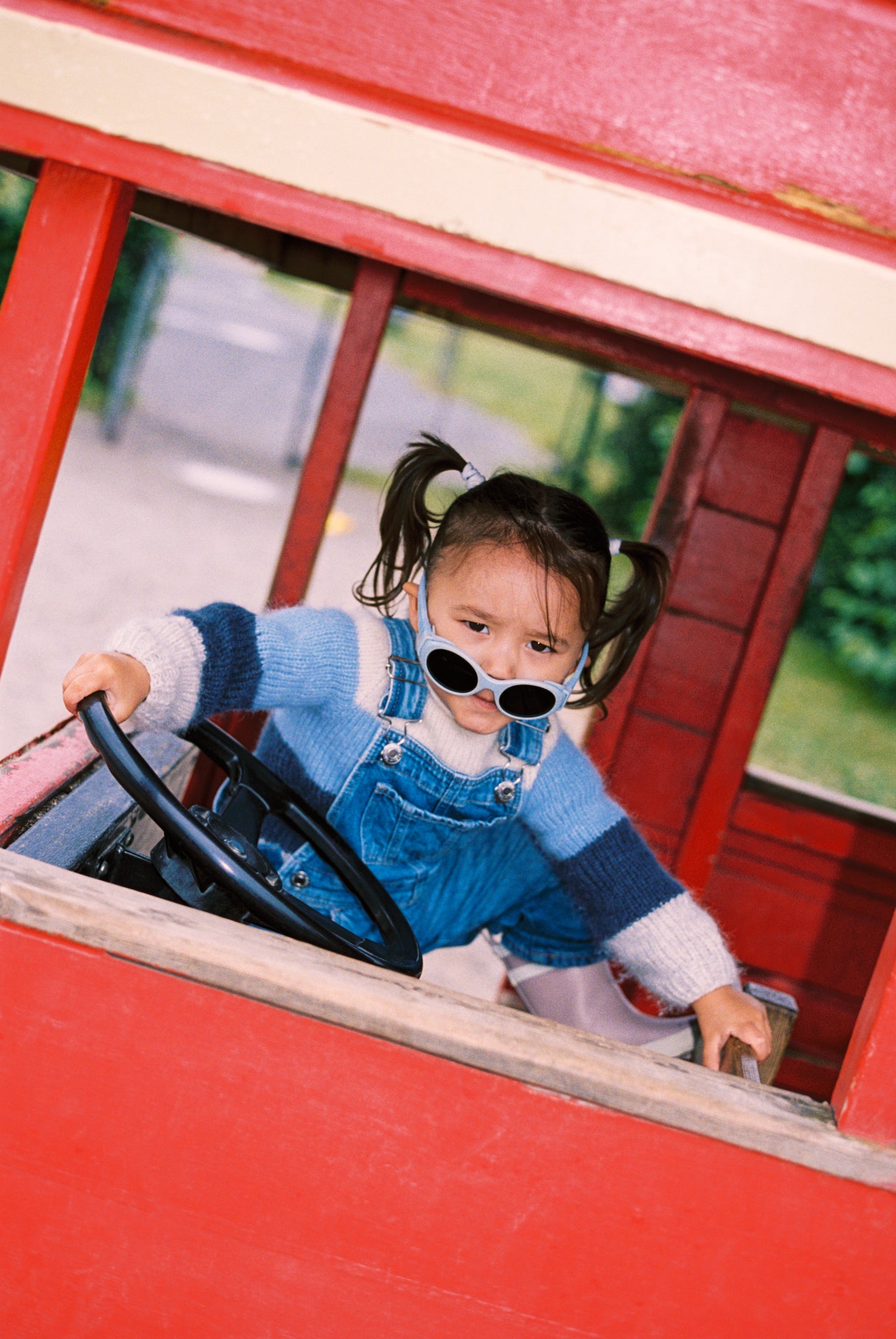 Child playing inside a red toy bus with Mokki sunglasses on