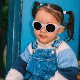 Child wearing Mokki Click & Change sunglasses and a blue outfit sitting on a playground slide.