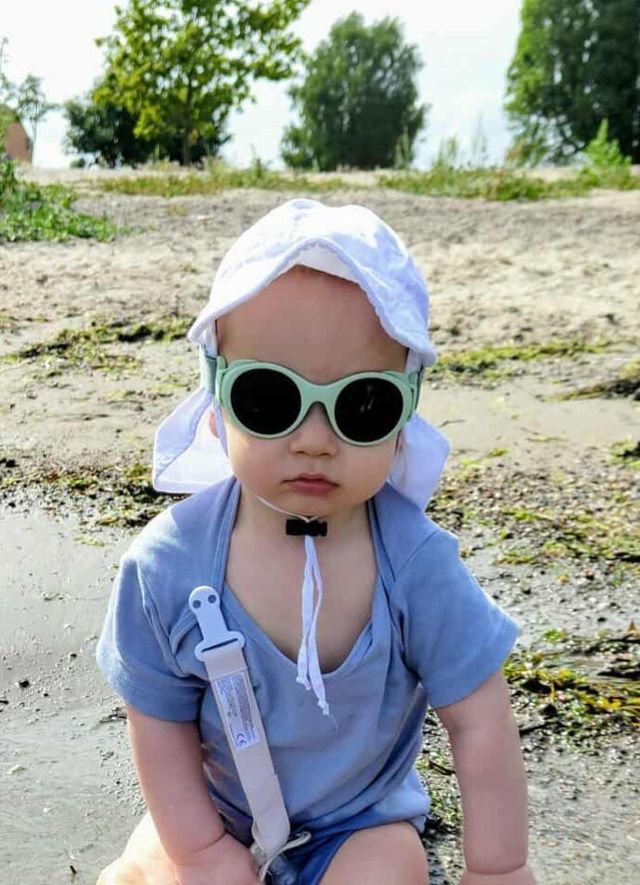 Child wearing green Mokki Click & Change  sunglasses sitting on a beach