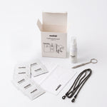 Mokki cleaning kit with an open cardboard box, spray bottle, pouches, cloth, and a black strap on a clean white background.