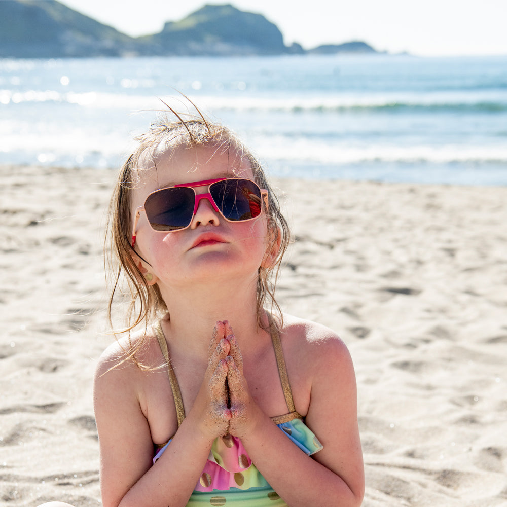 Young girl at the beach wearing Mokki Small 70s sunglasses in pink